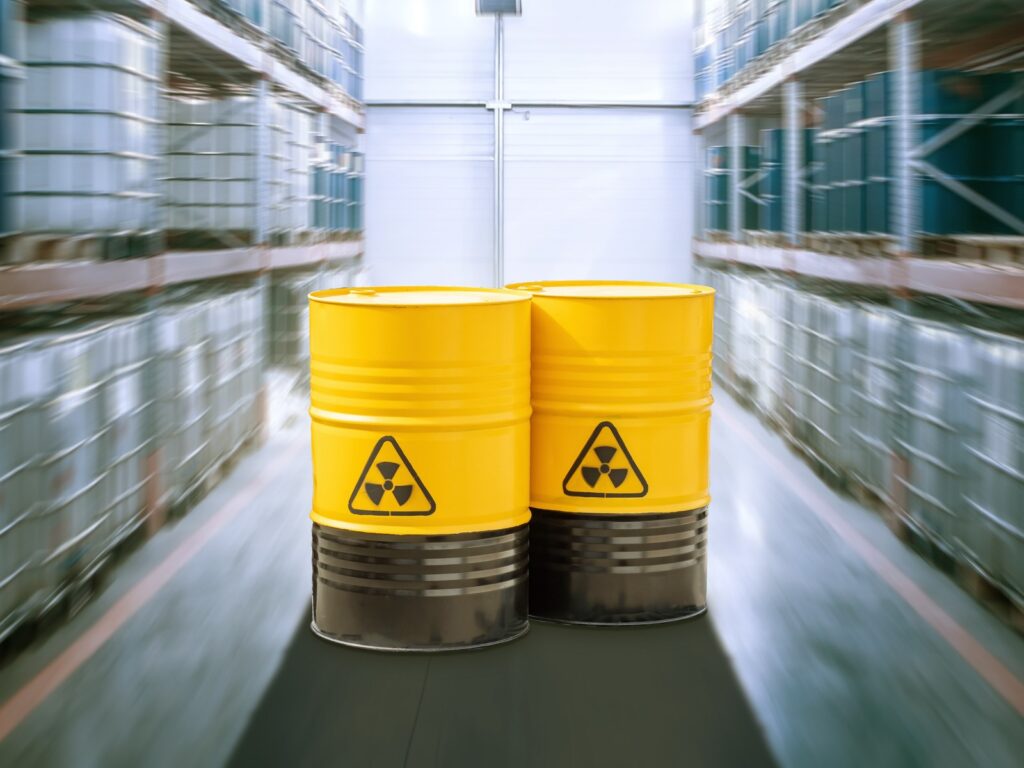 Rows of yellow barrels marked with radioactive warning labels stored in an industrial warehouse.