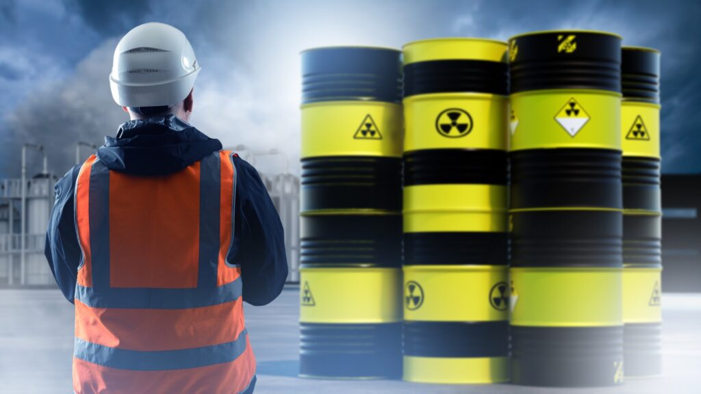 A worker standing near a row of barrels marked with radioactive warning symbols in an industrial facility.
