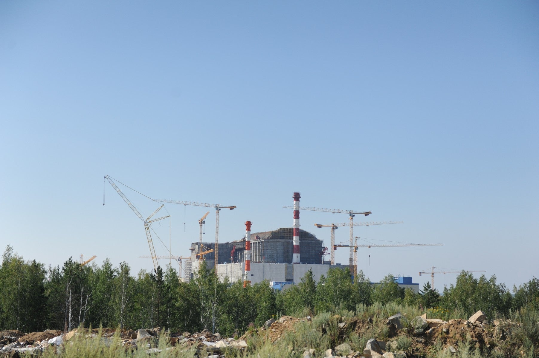An aerial view of a large industrial construction project with cranes and a partially built reactor structure.