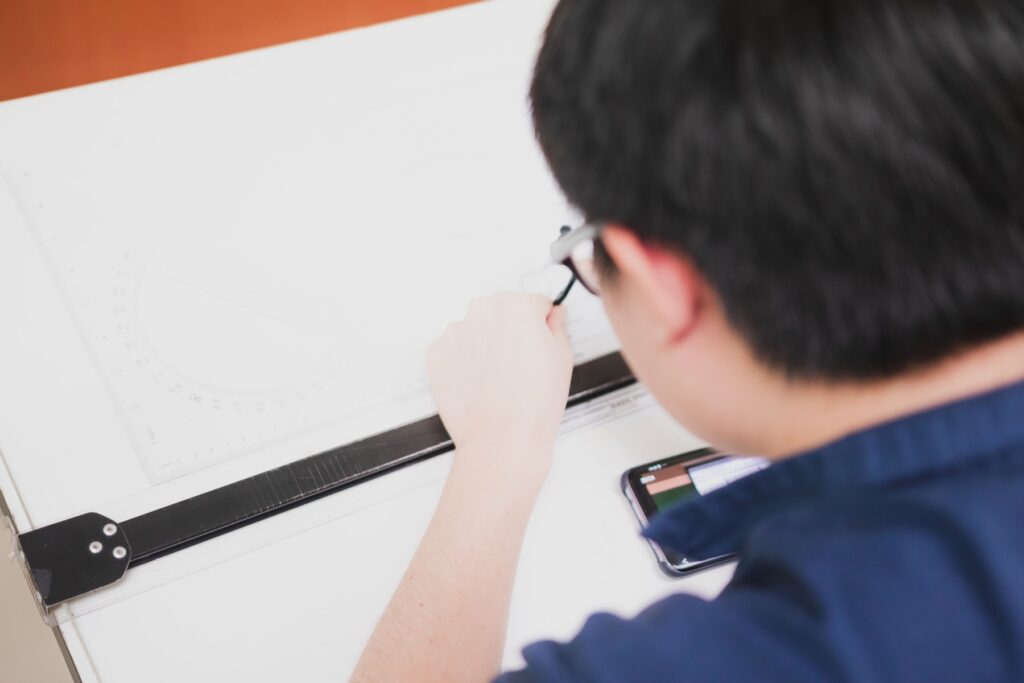 An engineer in uniform reviewing and sketching a technical blueprint at a design office.
