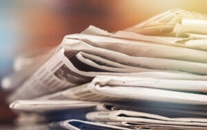 A close-up view of a thick stack of folded newspapers with blurred text visible on the pages.